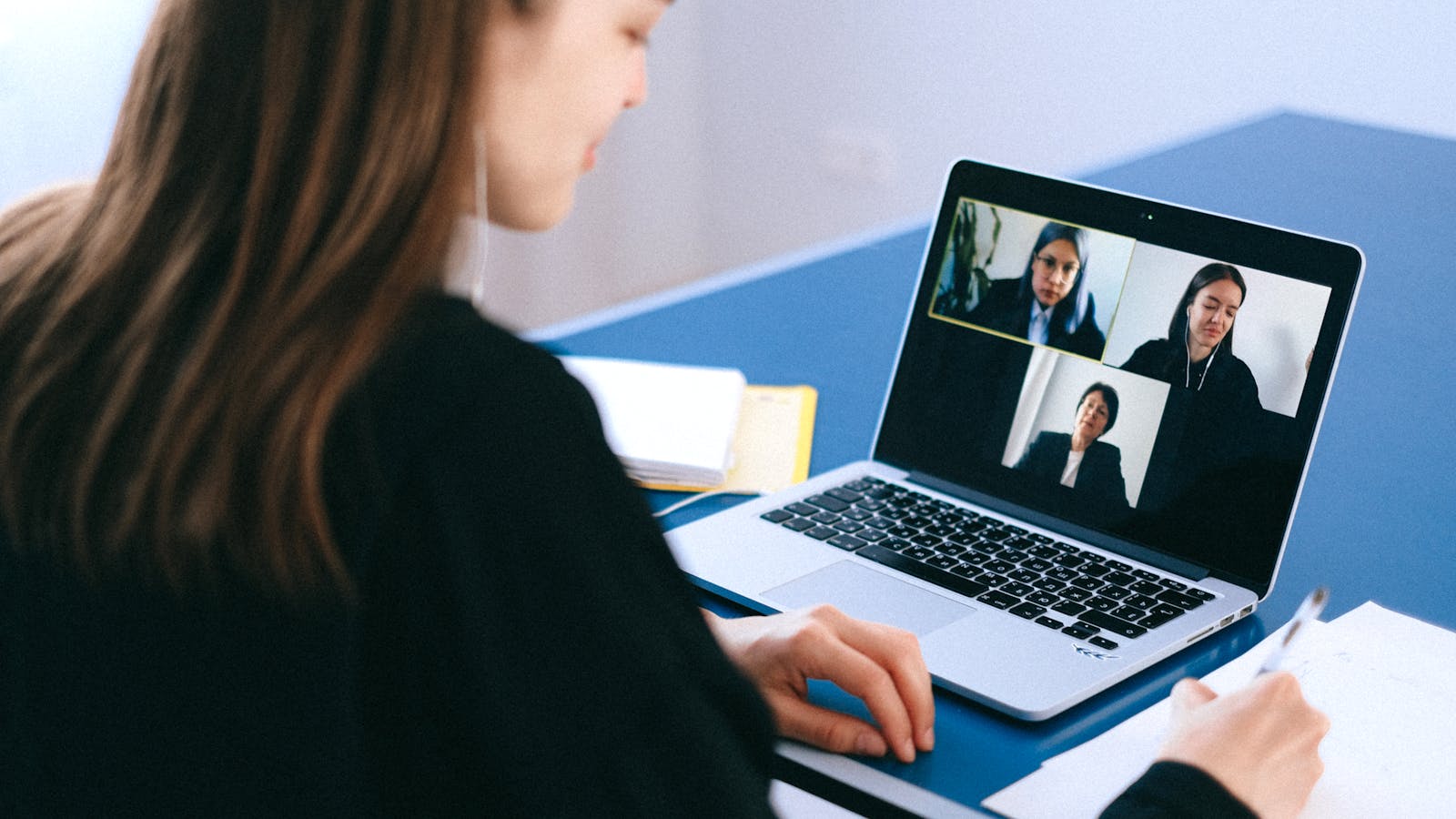 A young woman on a video meeting at her desk with headphones on.