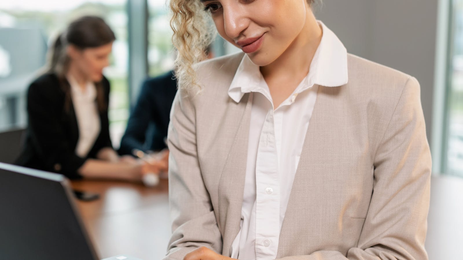 A young woman working on a laptop in a busy open plan office.
